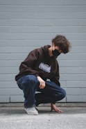 man in black hoodie and blue denim jeans sitting on gray concrete wall
