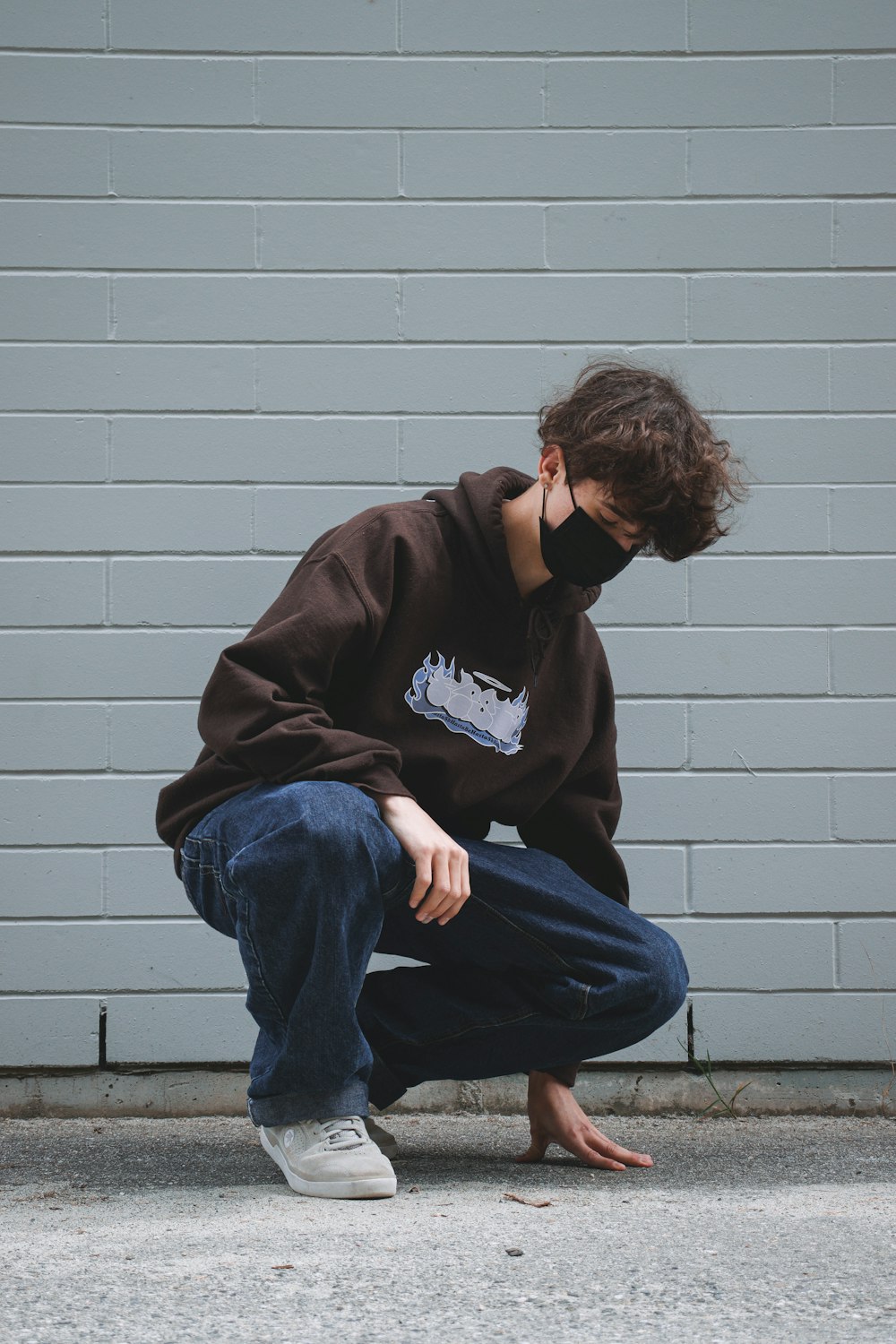 man in black hoodie and blue denim jeans sitting on gray concrete wall