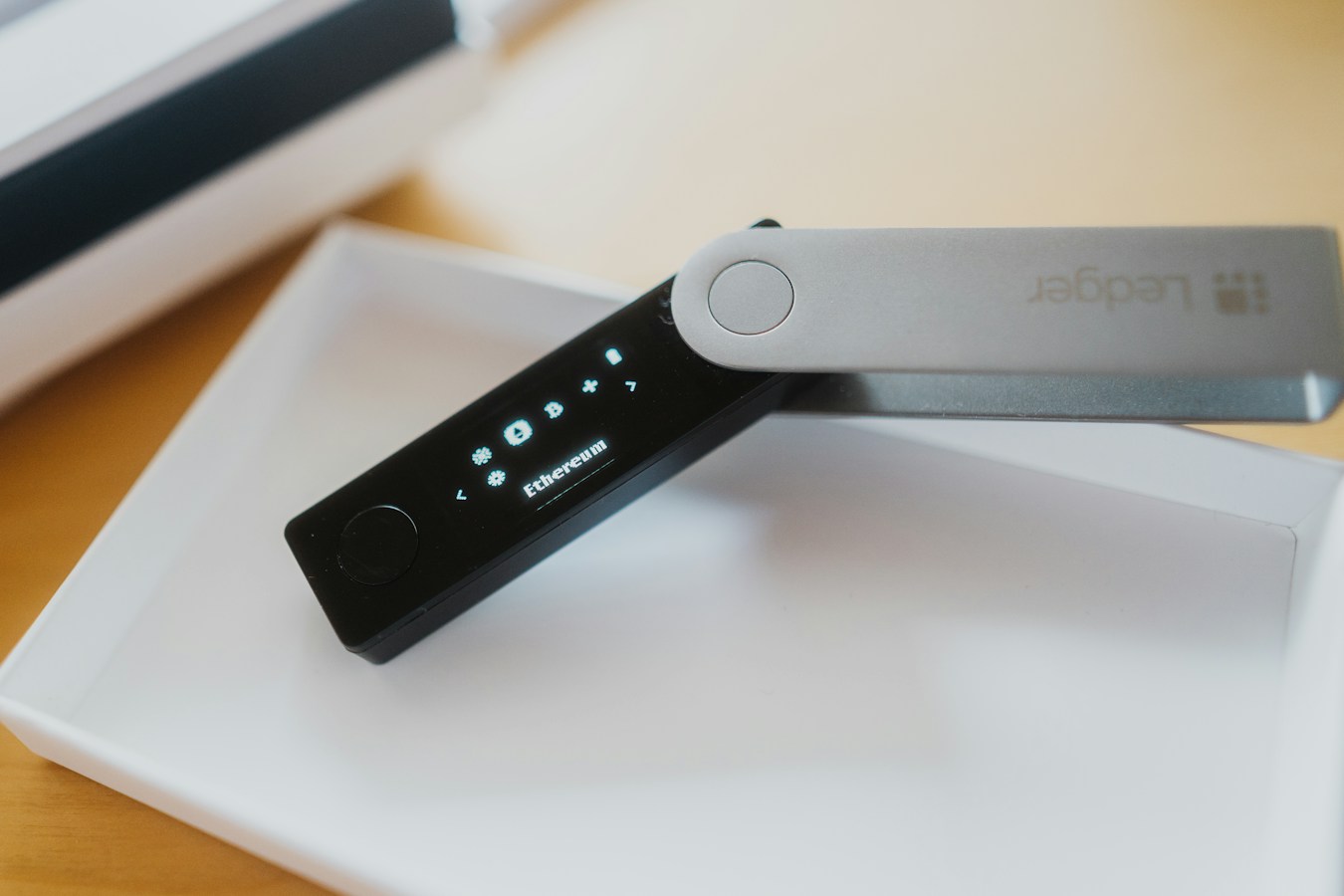 A black-and-silver Ledger hardware wallet resting in its white tray, its small oled screen lit up showing icons and the word 'Ethereum'