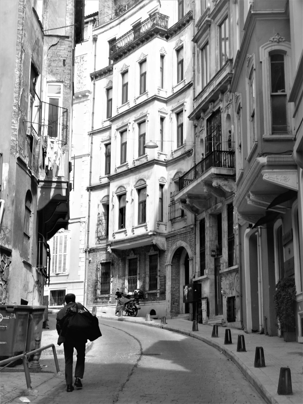 grayscale photo of man in black jacket walking on street