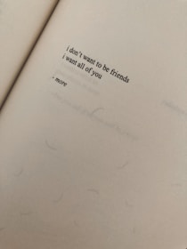 A close-up view of a page from a book featuring a short poem with the words 'i don't want to be friends, i want all of you - more'. The paper has a textured appearance and appears to be aged or slightly discolored.