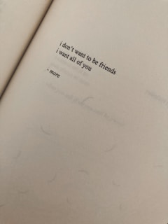 A close-up view of a page from a book featuring a short poem with the words 'i don't want to be friends, i want all of you - more'. The paper has a textured appearance and appears to be aged or slightly discolored.