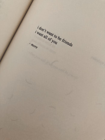 A close-up view of a page from a book featuring a short poem with the words 'i don't want to be friends, i want all of you - more'. The paper has a textured appearance and appears to be aged or slightly discolored.