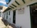 A quaint white building with green window and door frames, featuring a sign that reads 'la moraleja - villa de leyva.' The building has a rustic stone path in front, and pots with plants are visible. Bright string lights are hanging near the entrance.