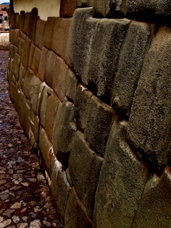 A detailed stone wall constructed with irregularly shaped and tightly fitted stones, characteristic of ancient architecture. The stones have a weathered appearance with a smooth, patinated surface. The cobblestone path runs alongside the wall.