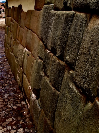 A detailed stone wall constructed with irregularly shaped and tightly fitted stones, characteristic of ancient architecture. The stones have a weathered appearance with a smooth, patinated surface. The cobblestone path runs alongside the wall.