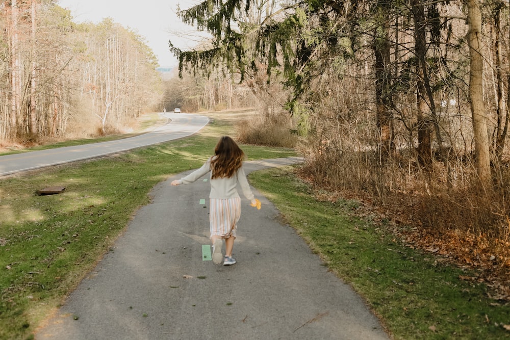 girl in white shirt walking on gray asphalt road during daytime