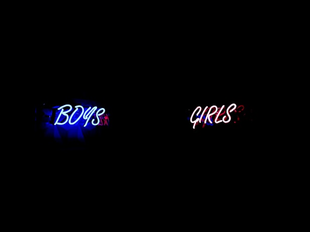 Neon signs reading 'BOYS' in blue and 'GIRLS' in red, symbolizing gender disparities 