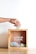 A hand is placing a banknote into a wooden donation box, which contains various other banknotes and coins. The box has 'Sedekah Shubuh' written on it along with a social media handle.