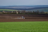 A wide shot of a tractor working on a green farm landscape.