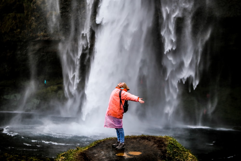 昼間、滝の近くの岩の上に立つ青いジャケットの女性