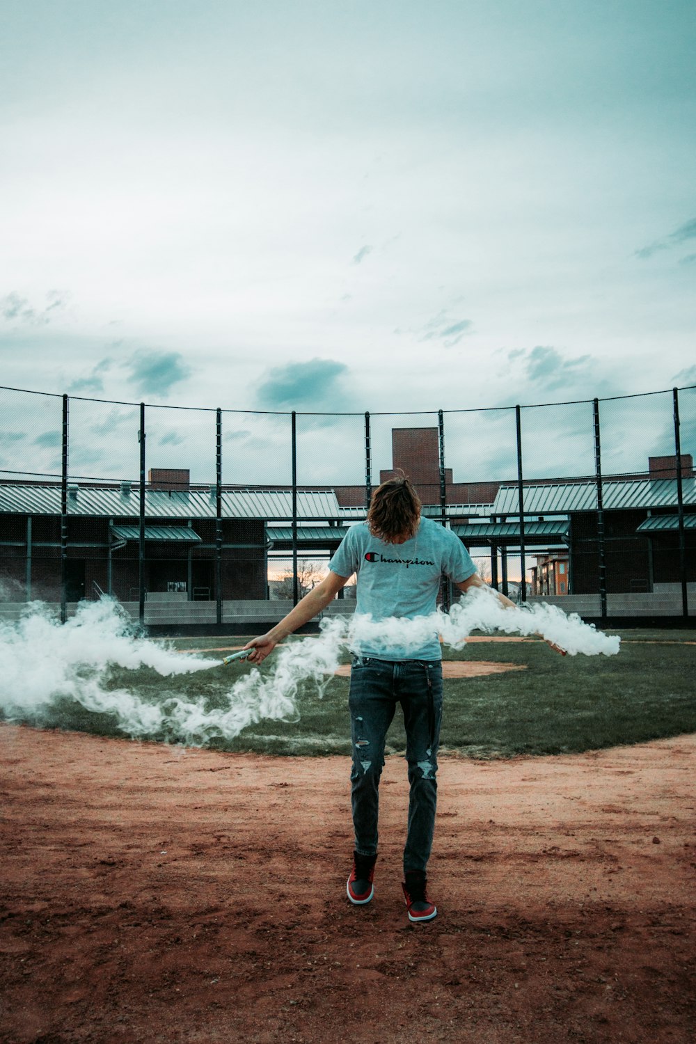 woman in blue denim jeans standing on brown field near gray metal fence during daytime