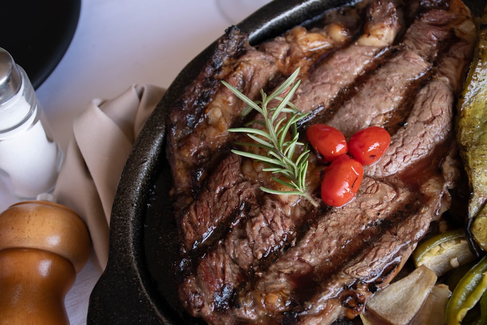 grilled meat with tomato and green vegetable on black pan