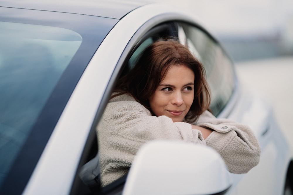 woman in gray coat leaning on white car