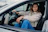 Smiling woman in a pink jacket sitting confidently in the driver's seat of a car.