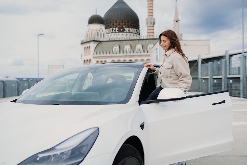 woman in gray blazer standing beside white car