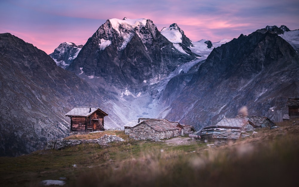 brown wooden house on green grass field near snow covered mountain during daytime