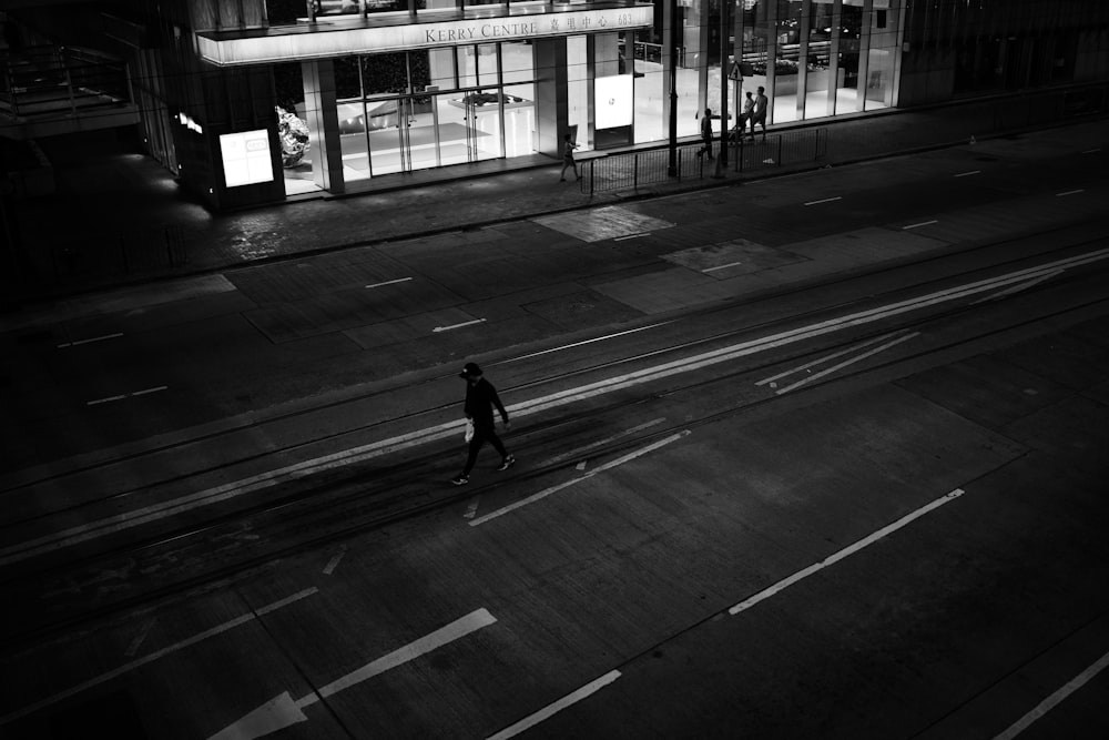 grayscale photo of man walking on sidewalk