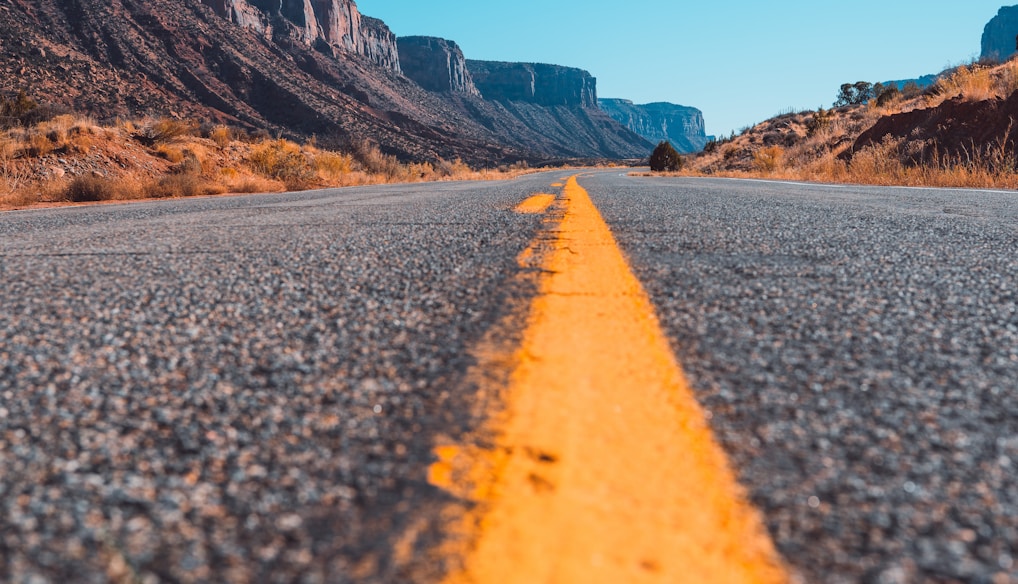 gray concrete road near brown rocky mountain during daytime