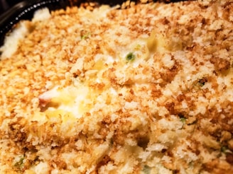 A close-up view of a baked dish with a golden-brown, crumbly topping. The surface appears crispy with visible green peas peeking through the breaded layer, suggesting a casserole or gratin. The texture is inviting and suggests a warm, freshly-baked meal.