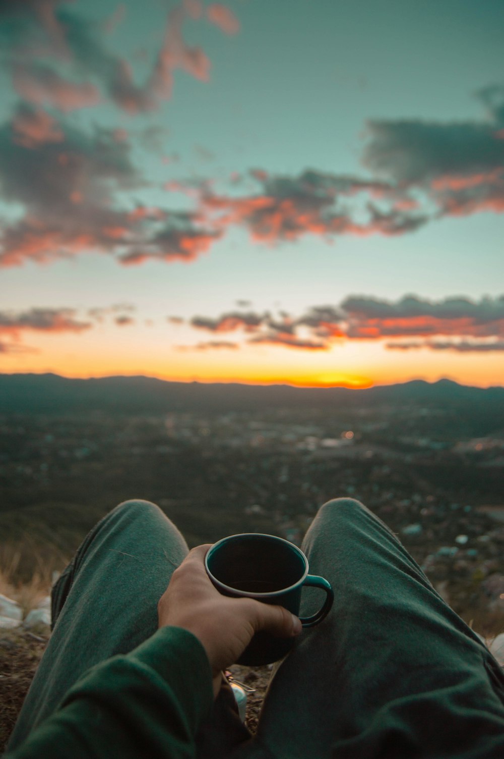 person in black pants holding black ceramic mug during sunset