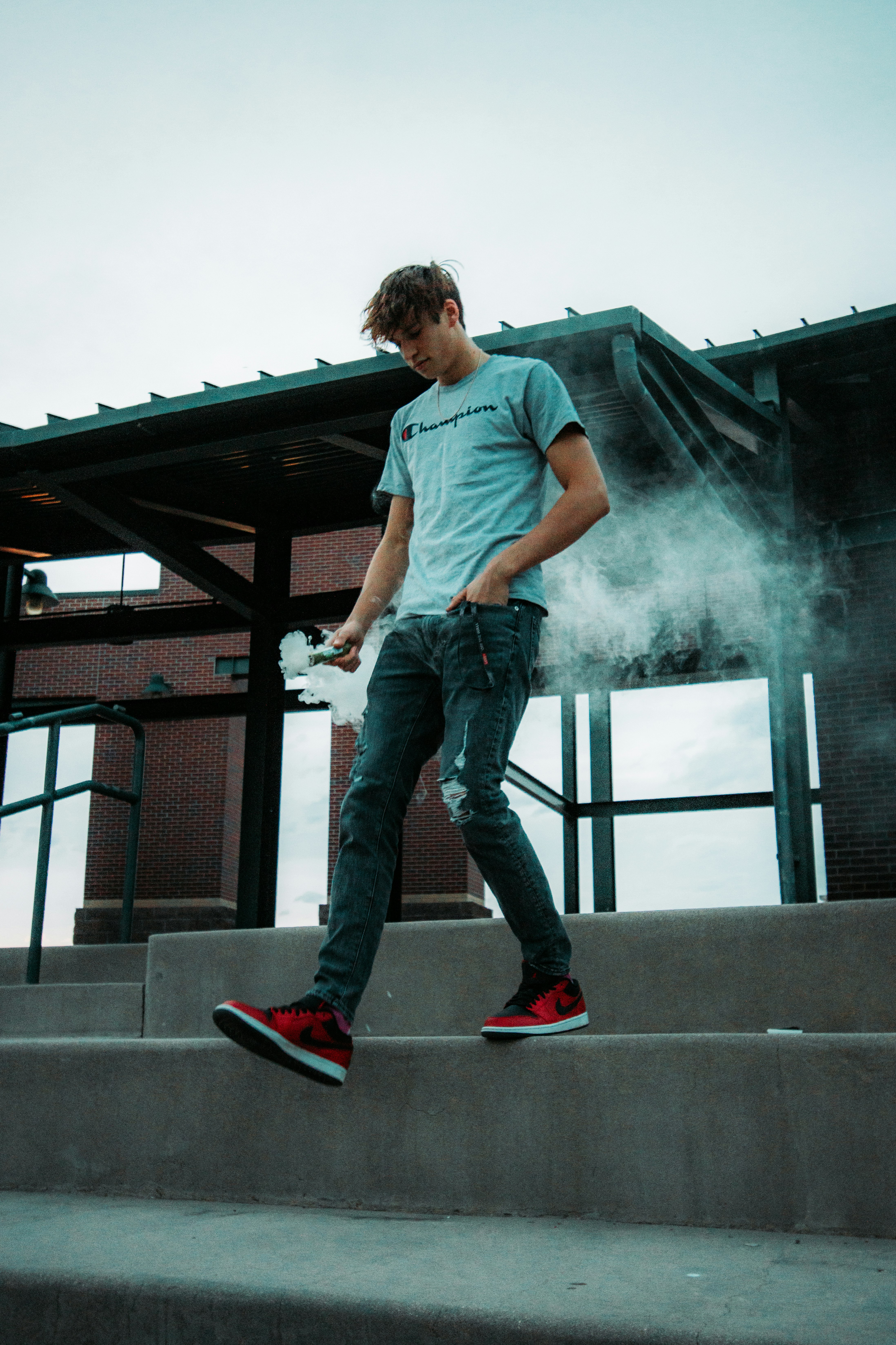 man in blue t-shirt and blue denim jeans standing on gray concrete stairs