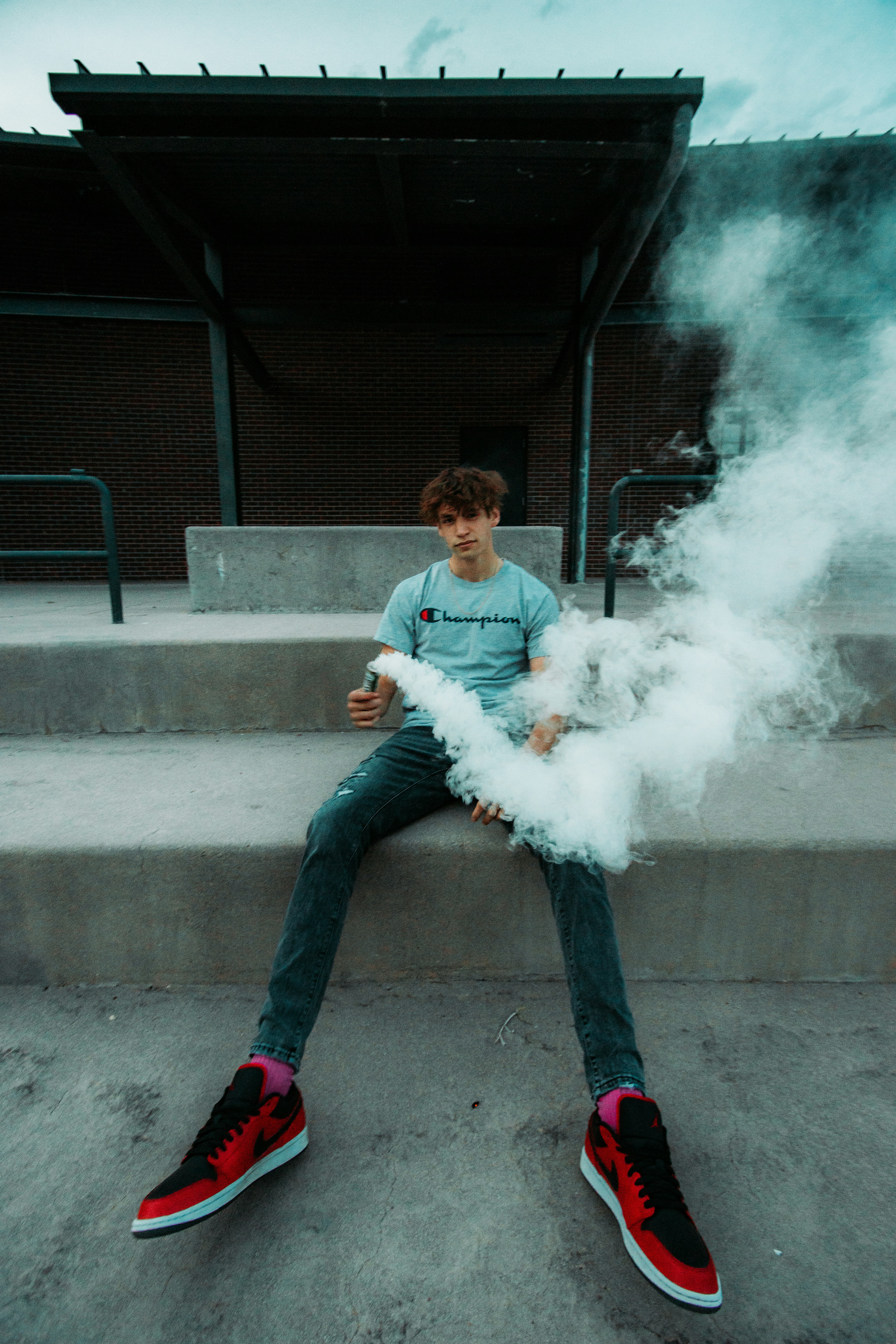 man in white long sleeve shirt and blue denim jeans sitting on concrete bench smoking