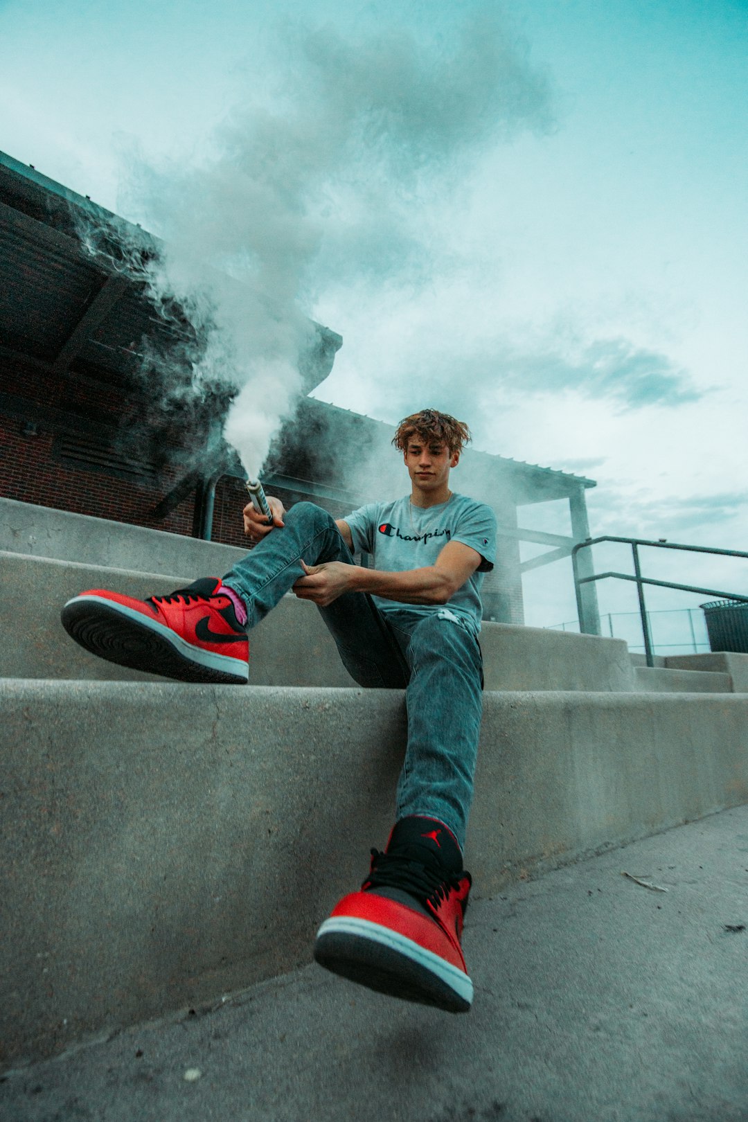 man in gray t-shirt and blue denim jeans sitting on concrete wall