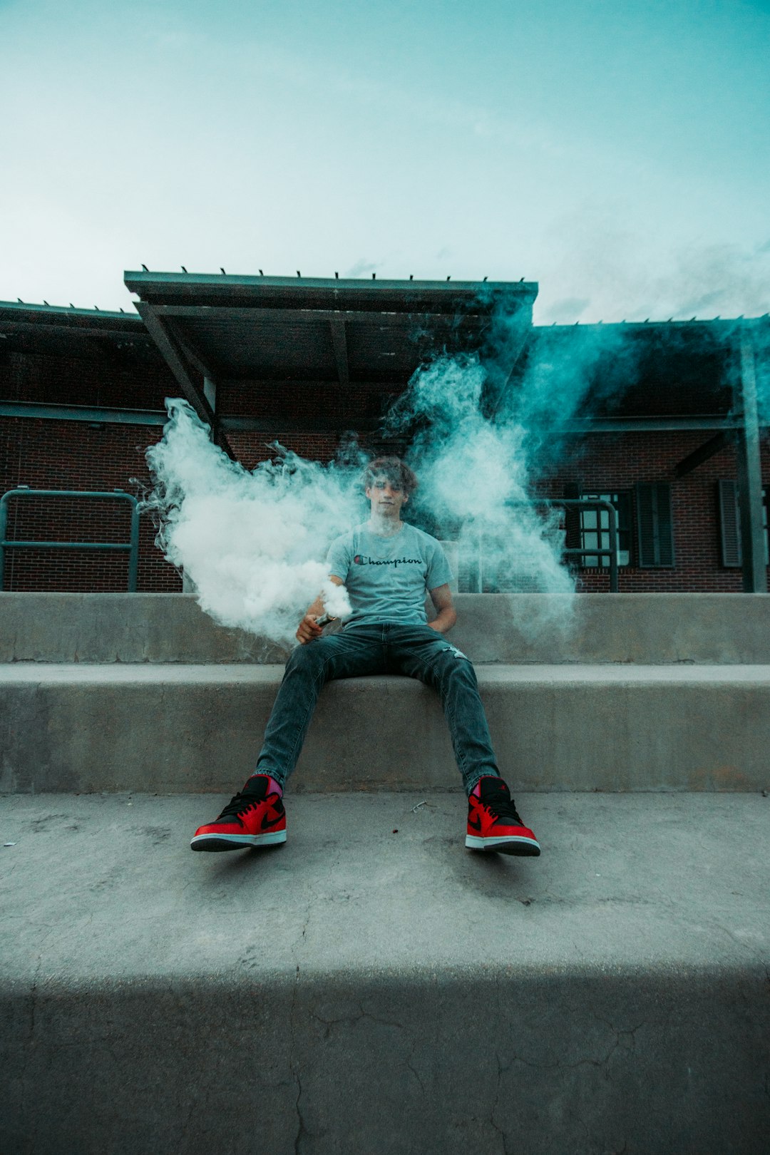 man in blue denim jeans and red sneakers sitting on concrete stairs with green smoke