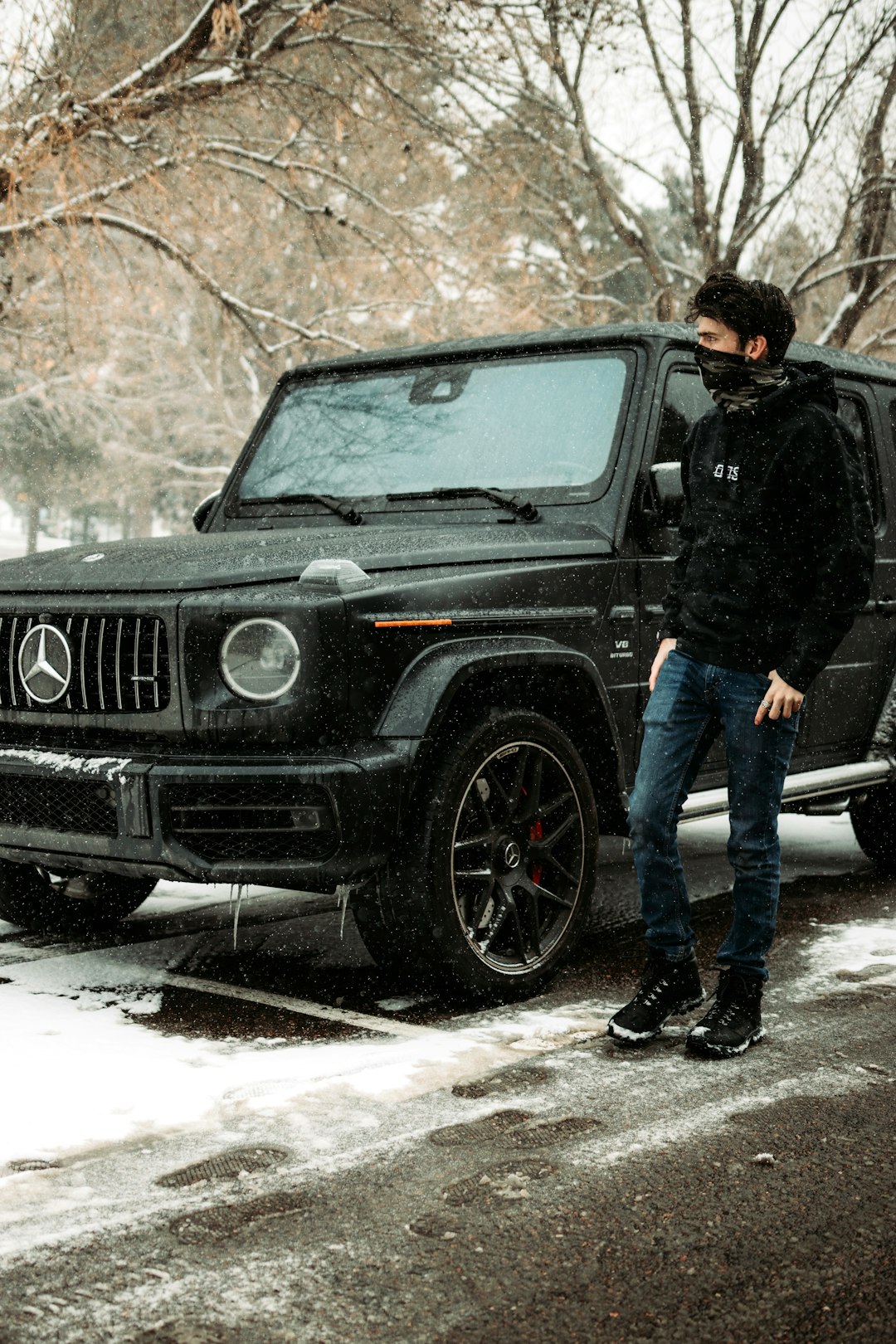 man in black jacket and blue denim jeans standing beside black jeep wrangler