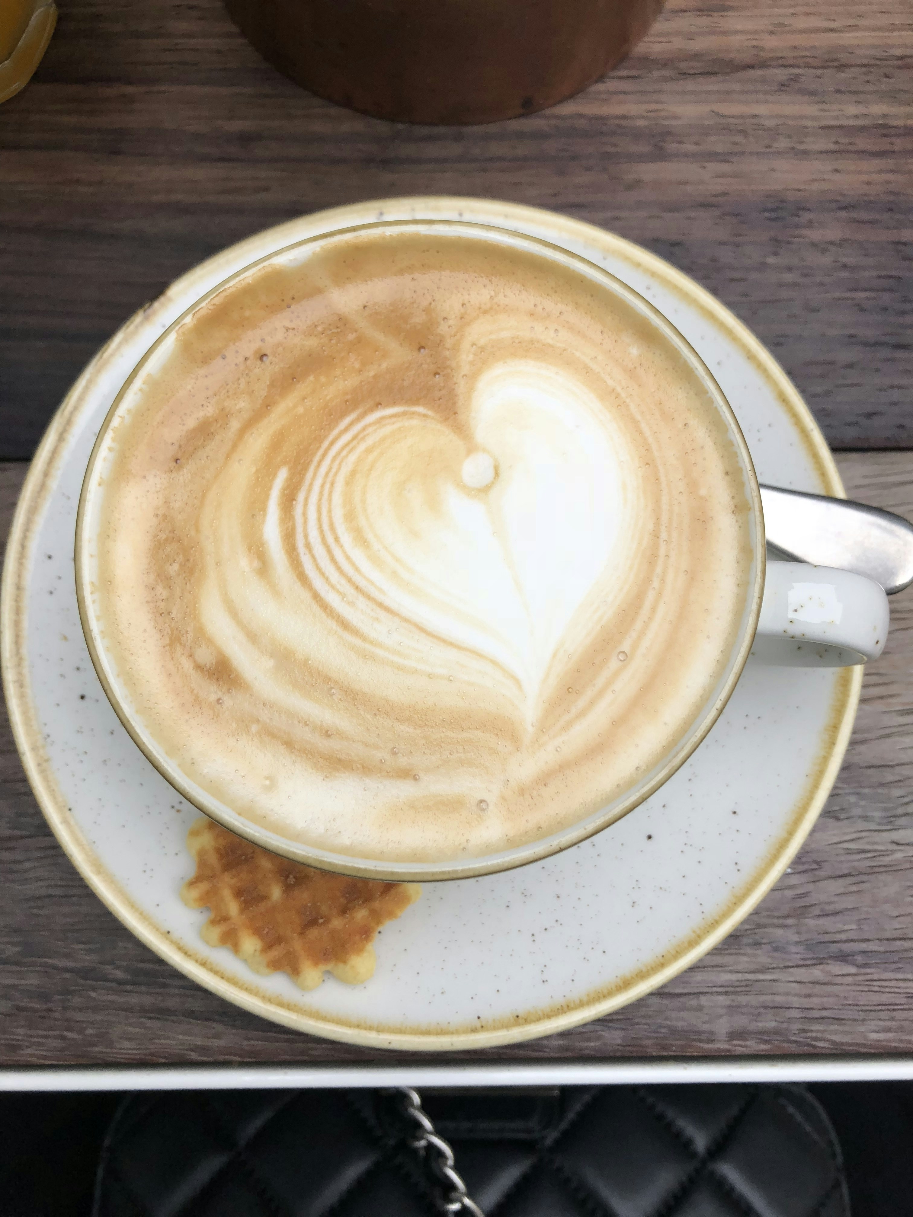 Warm cup of coffee with latte art, resting on a wooden counter beside a plate of freshly made waffles dusted with powdered sugar