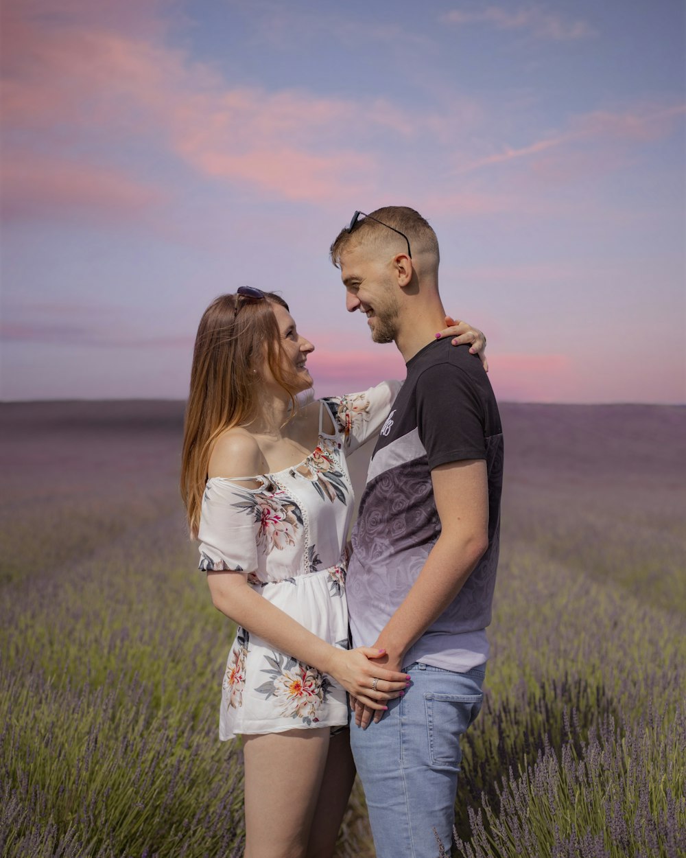 man in black crew neck t-shirt kissing woman in white floral dress on green grass