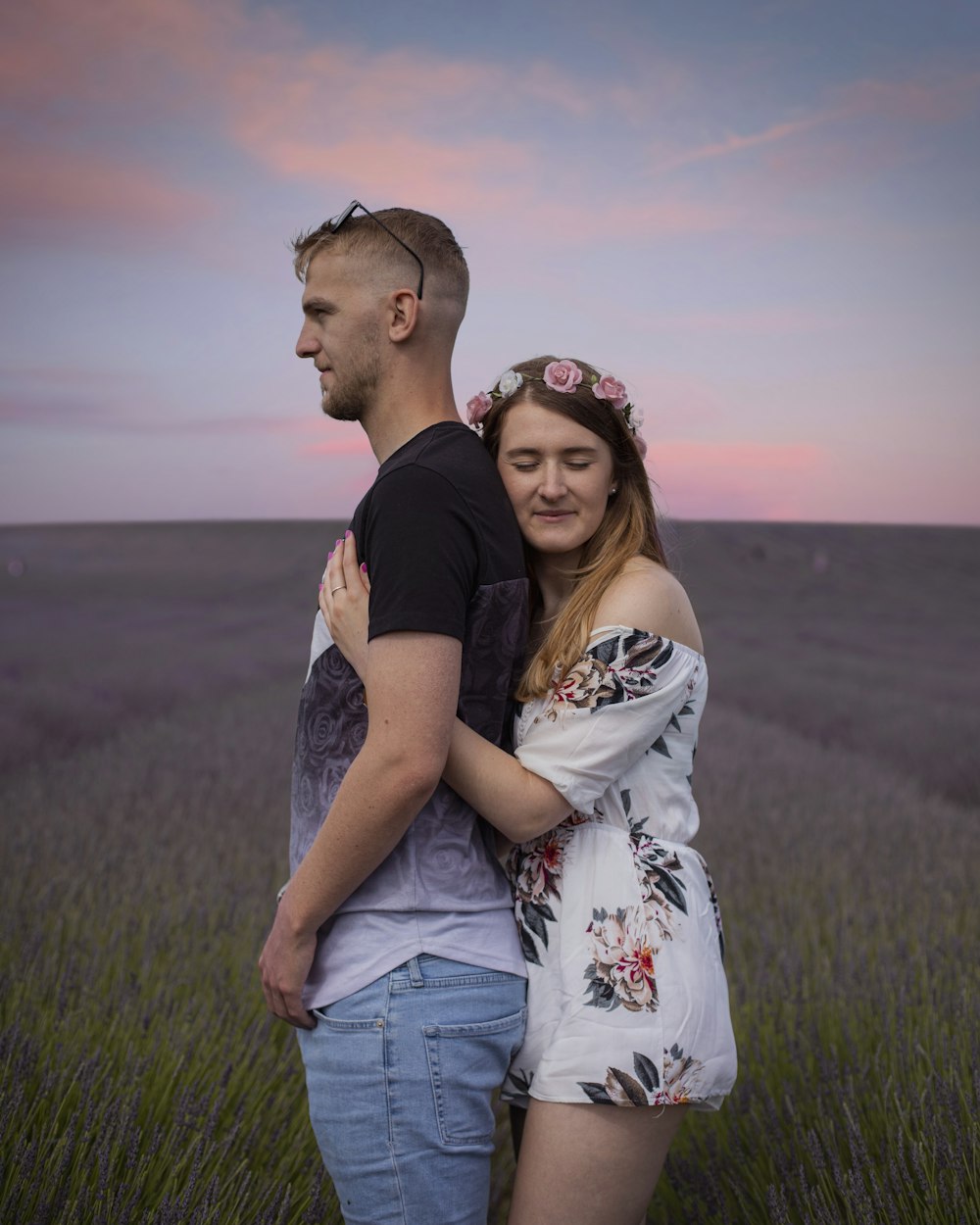 man in black crew neck t-shirt kissing woman in white floral dress on green grass