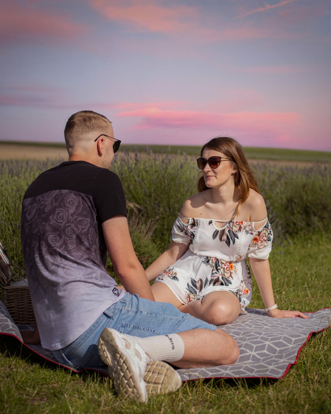 man and woman sitting on red and white textile on green grass field during daytime