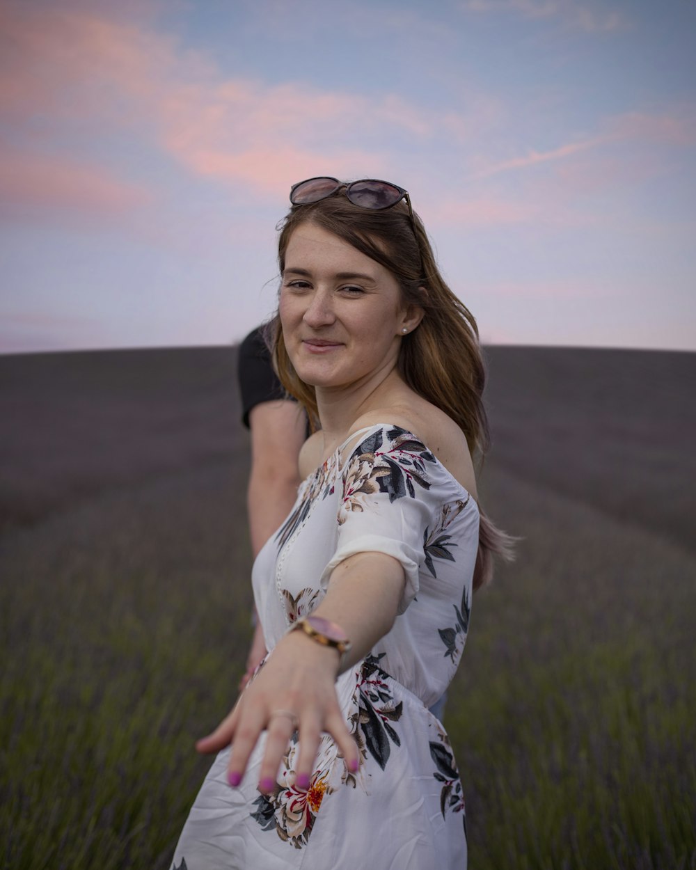 donna in abito floreale bianco e nero in piedi sul campo di erba verde durante il giorno