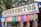 A colorful street vendor sign displaying a variety of candy or snack items, each wrapped in clear packaging and clipped to a string. The sign above reads 'Ricos Chitos, Preparados con Chile, Sal y Limon' in bold letters. The background features green trees, suggesting an outdoor setting.