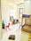 A small, bright room with a tiled floor, containing children's furniture such as colorful plastic chairs, a small table, and a bunk bed. The walls have educational materials like alphabet cutouts and whiteboards with scribbles. Various items, including a chalkboard, cushion, and water bottle, are scattered around.