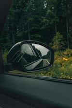 car side mirror reflecting green trees during daytime
