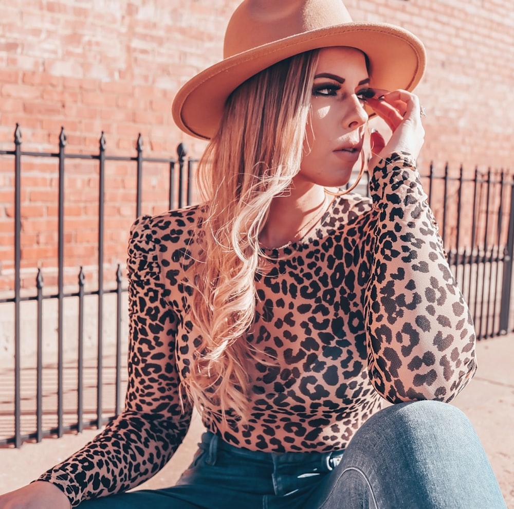 woman in brown and black leopard long sleeve shirt and blue denim jeans sitting on brown