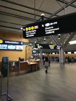 The interior of an airport terminal includes signage for Canadian flights, check-in counters, and an information desk. A person is walking towards the check-in area, and there are several illuminated signs providing directions. The setting is clean and modern with high ceilings.