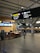 The interior of an airport terminal includes signage for Canadian flights, check-in counters, and an information desk. A person is walking towards the check-in area, and there are several illuminated signs providing directions. The setting is clean and modern with high ceilings.