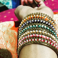 A close-up of a woman’s hand adorned with delicate gold-toned bangles and rings, set against a soft white background.