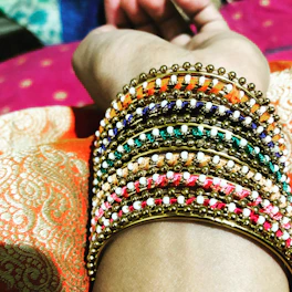 Close-up of colorful handmade thread bangles arranged in a circle on a soft pastel fabric.
