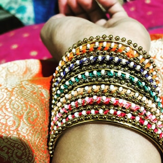 A hand adorned with multiple gold bangles against a neutral backdrop.