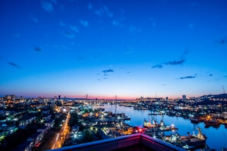 A vibrant Asian city skyline at dusk with cargo ships docked at the harbor.