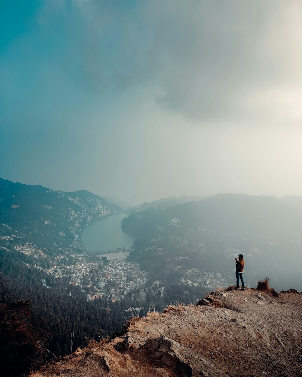 person standing on rock formation looking at the lake