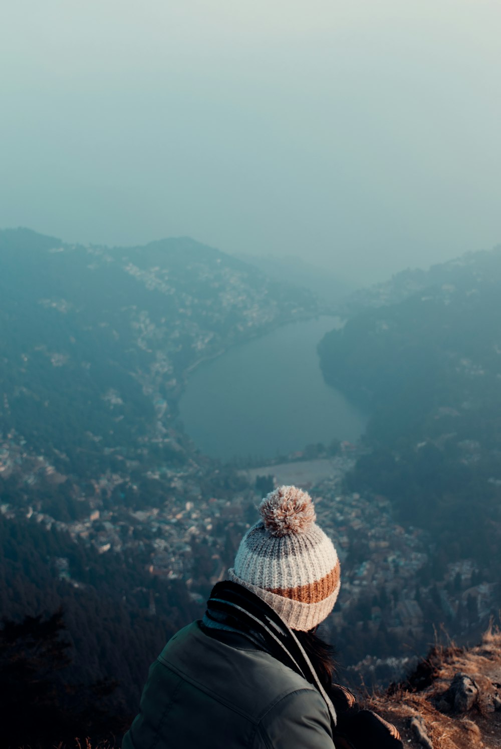 person in black jacket and brown and white plaid hat standing on top of the mountain