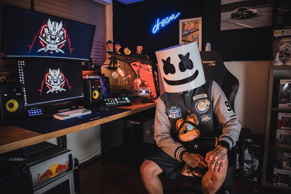 Person with a smiley face mask, at a computer, using royalty free music for Twitch