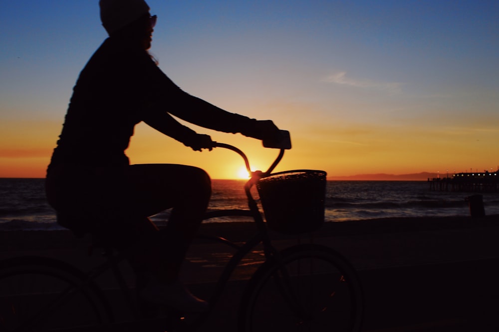 silhouette of man riding bicycle on beach during sunset