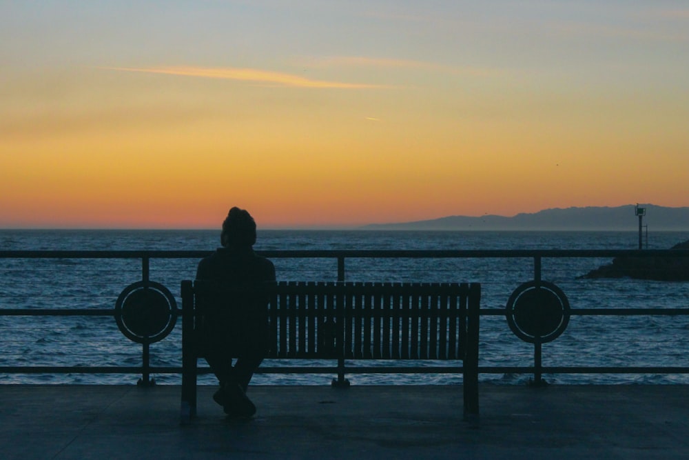 Silhouette der Person, die während des Sonnenuntergangs auf dem Dock steht